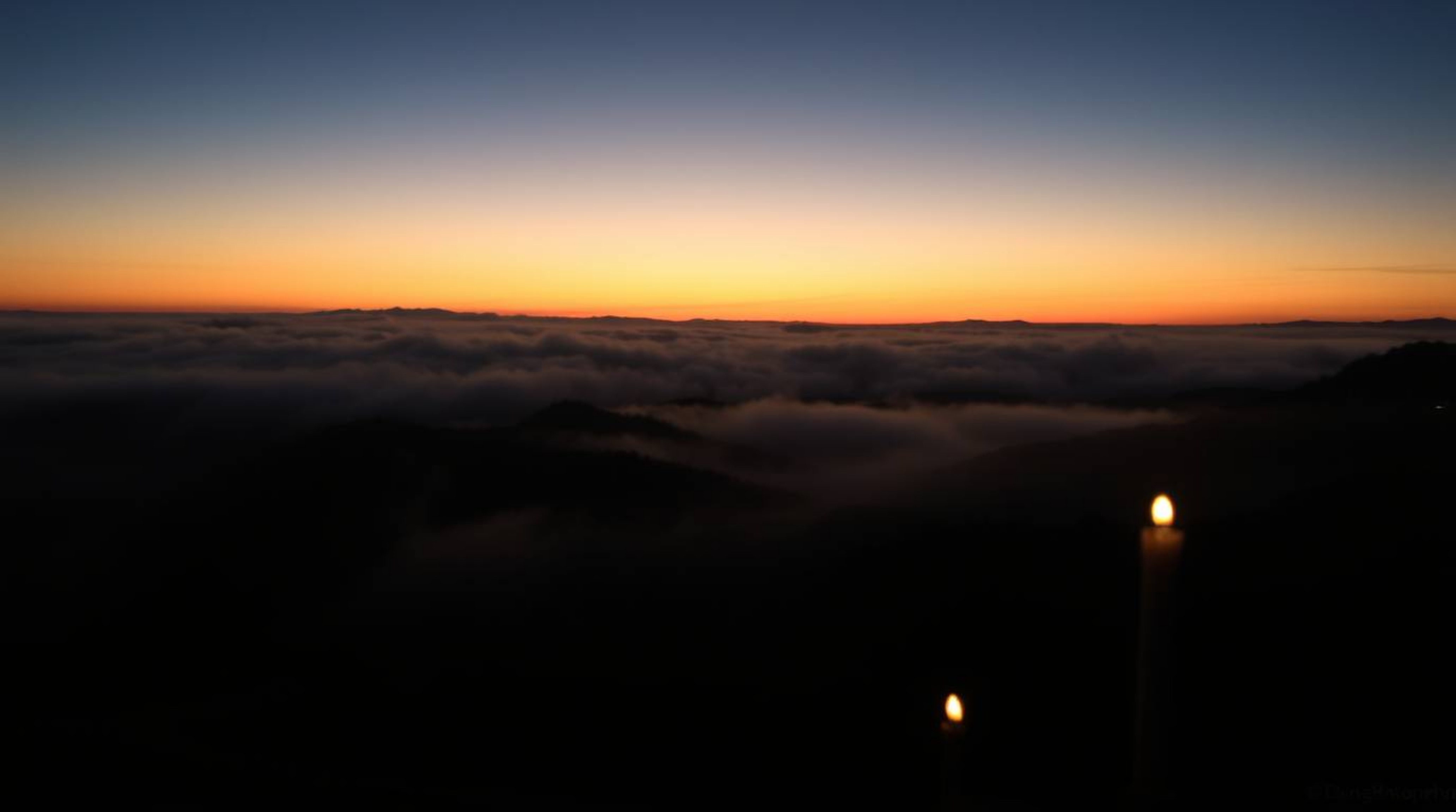 A captivating long-exposure photograph depicts fog-shrouded hills bathed in the warm glow of a setting sun.  Candlelight flic