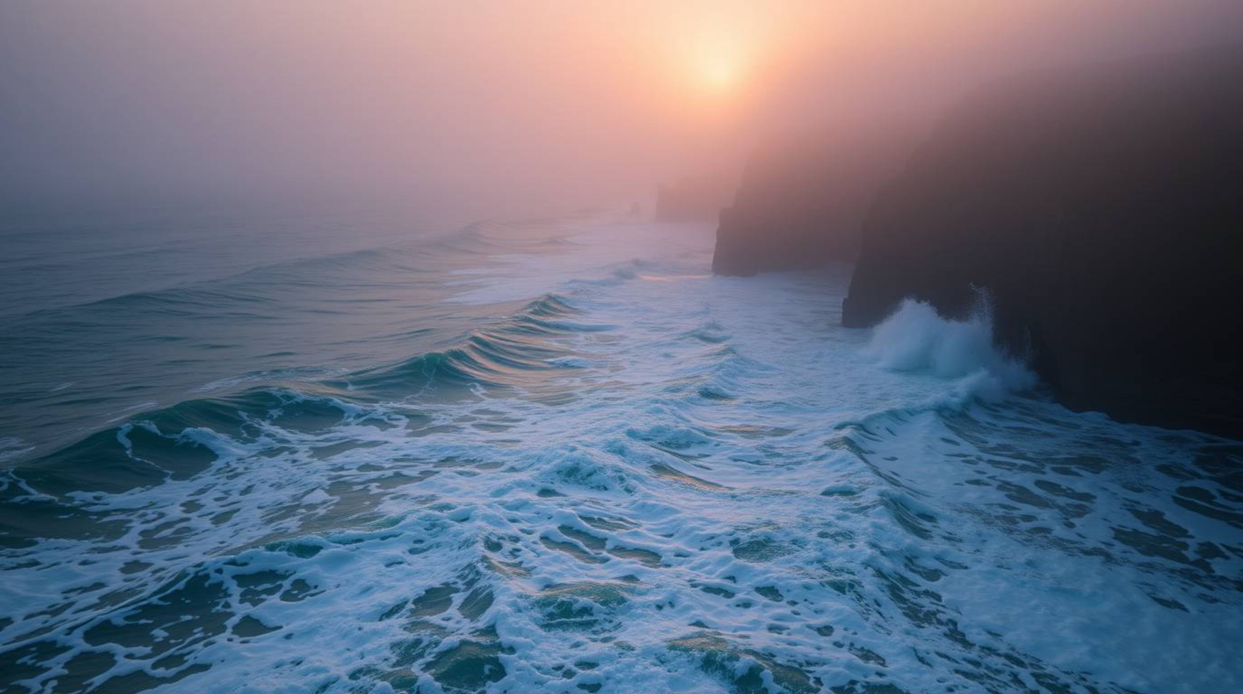 An extreme macro photograph captures the raw texture of waves crashing against cliffs at sunset.  Shrouded in thick fog, the 
