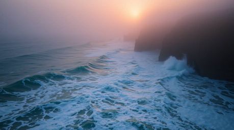 An extreme macro photograph captures the raw texture of waves crashing against cliffs at sunset.  Shrouded in thick fog, the 
