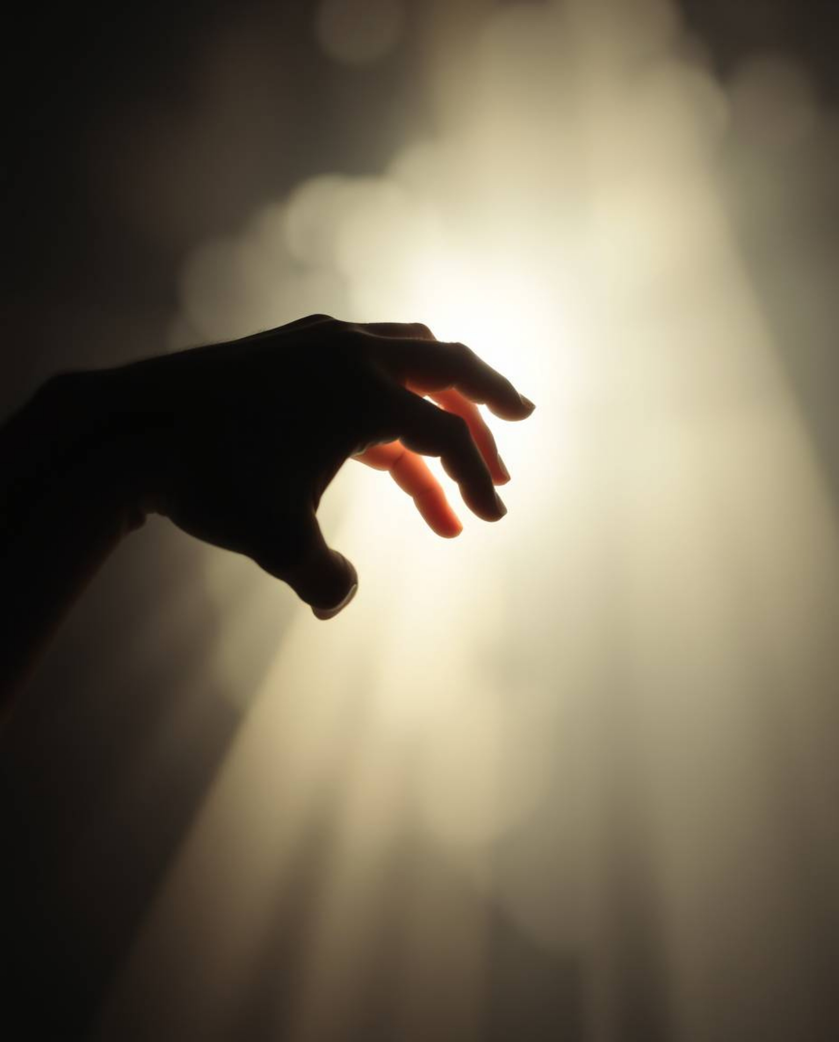 Capture a soft, dreamy atmosphere with volumetric lighting.  A hand reaches towards a light source emerging from darkness, cr