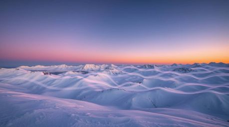 A captivating long exposure photograph showcases snow-covered mountains bathed in the glow of a pastel sunset.  Creative ligh