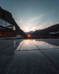A high-angle architectural photograph captures a sunset reflected in a glassy fjord. This wide-angle shot, taken from an elev