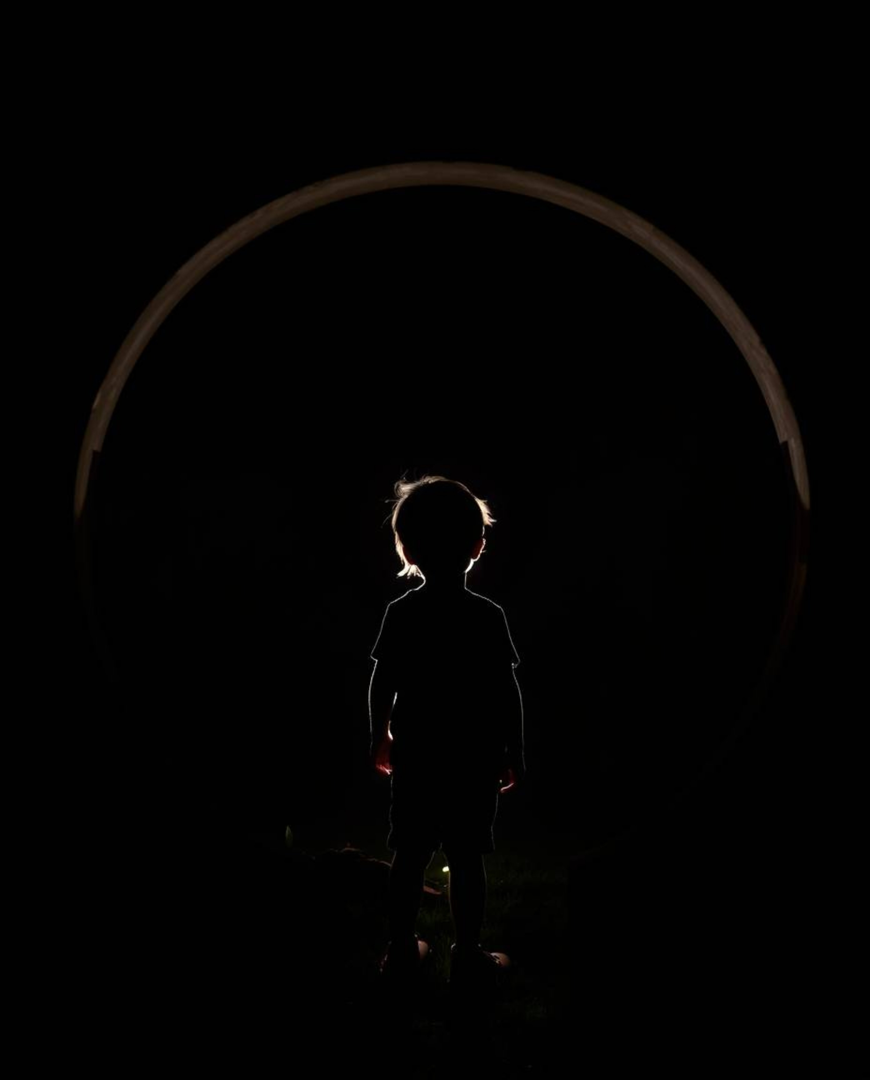 A captivating image of a child silhouetted against a glowing circular portal in their backyard.  The scene is dramatically li