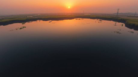 Capture the magic of a serene evening with this overhead bird's-eye view photograph of a calm pond reflecting a vibrant sunse