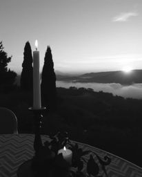 Classic black and white photograph: timeless elegant style, warm candlelight glow, flickering flames, Tuscany sunset over mis