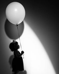 A timeless black and white image captures a child holding a balloon, dramatically lit by strong, hard light. The direct, hars