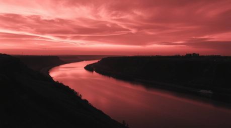 A timeless and elegant black and white photograph captures a winding river glowing under a dramatic orange-pink sunset.  The 