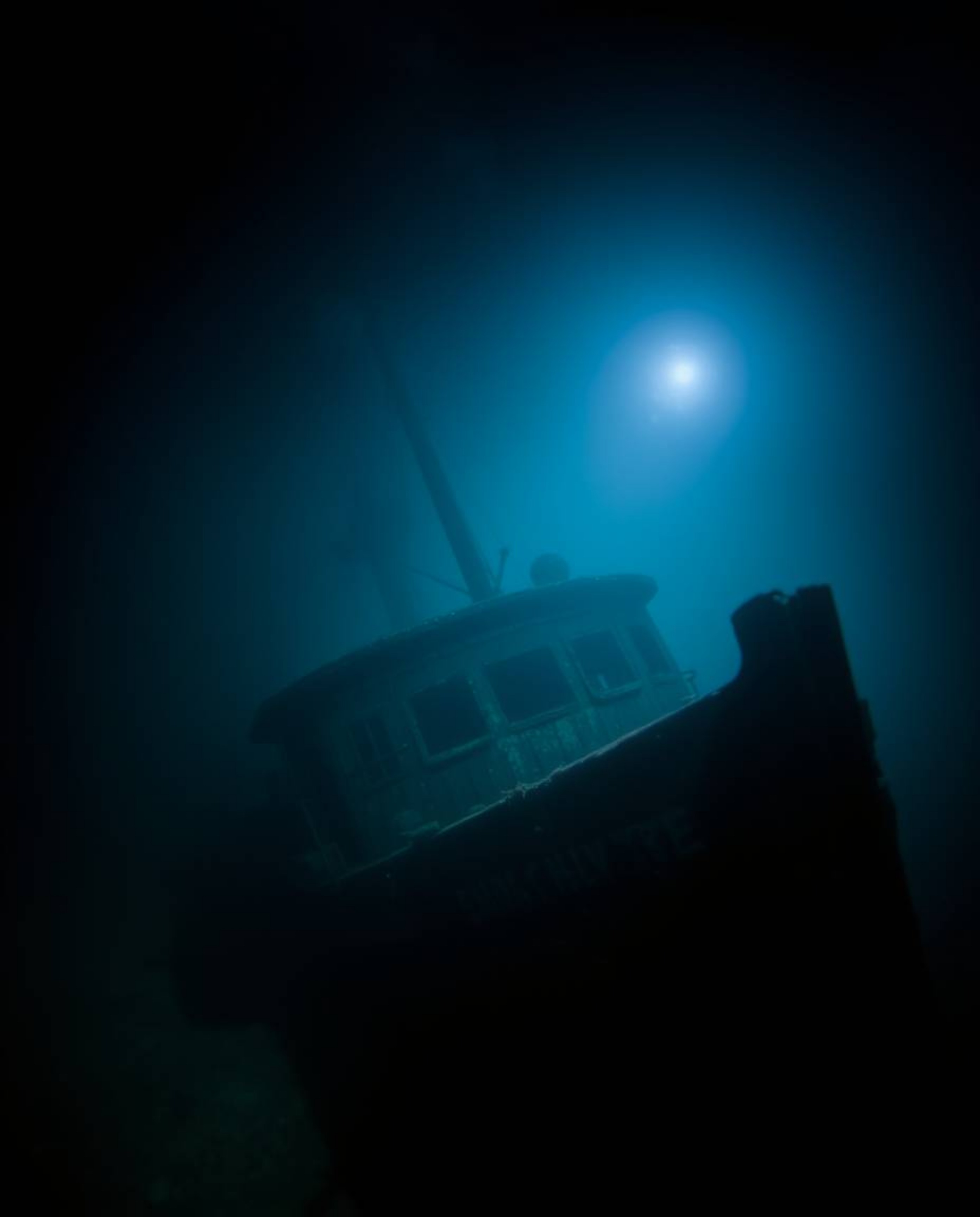 Discover a captivating underwater shipwreck photograph.  This moody image features a sharply focused wreck against a blurred 