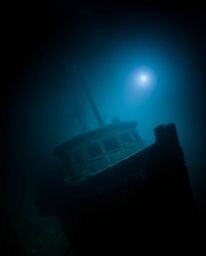 Discover a captivating underwater shipwreck photograph.  This moody image features a sharply focused wreck against a blurred 