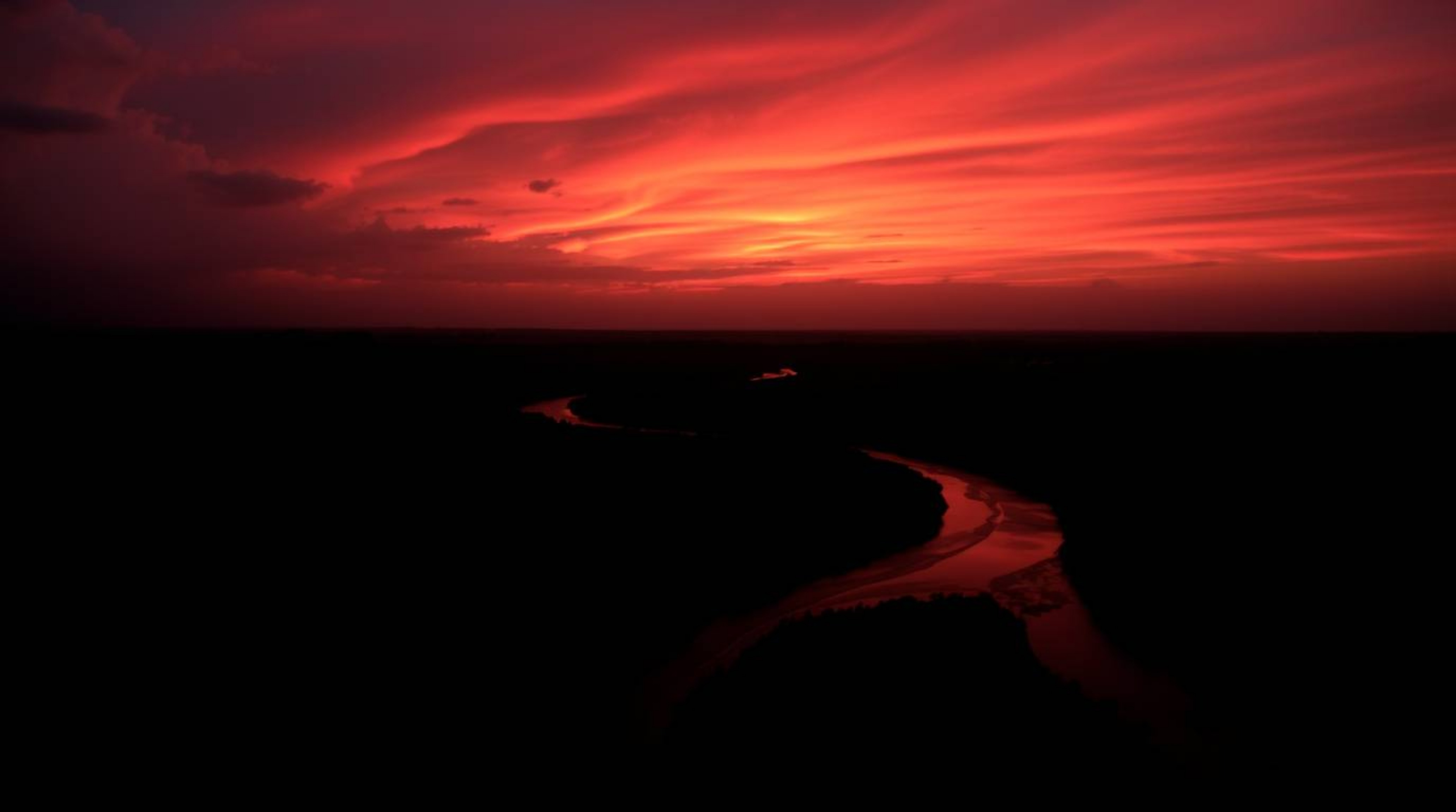 Witness a breathtaking landscape featuring a winding river shimmering beneath a dramatic orange-pink sky. The scene is render