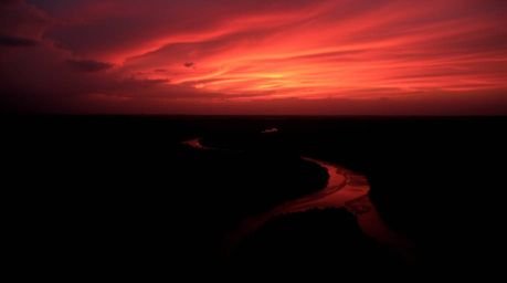 Witness a breathtaking landscape featuring a winding river shimmering beneath a dramatic orange-pink sky. The scene is render