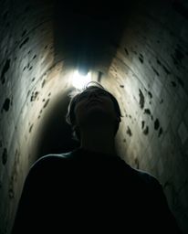 A captivating low-angle shot depicts a person with subtle features standing at the edge of a tunnel, their gaze directed upwa