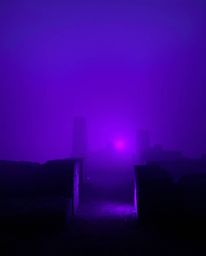 Deep ultraviolet hues and thick fog create a high-contrast, low-visibility scene at sunset. This dramatic setting illuminates