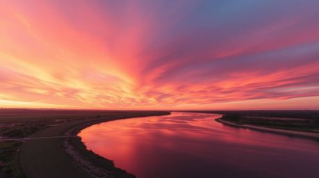 A breathtaking photograph capturing a winding river bathed in the warm glow of a dramatic orange-pink sky. The image is rende