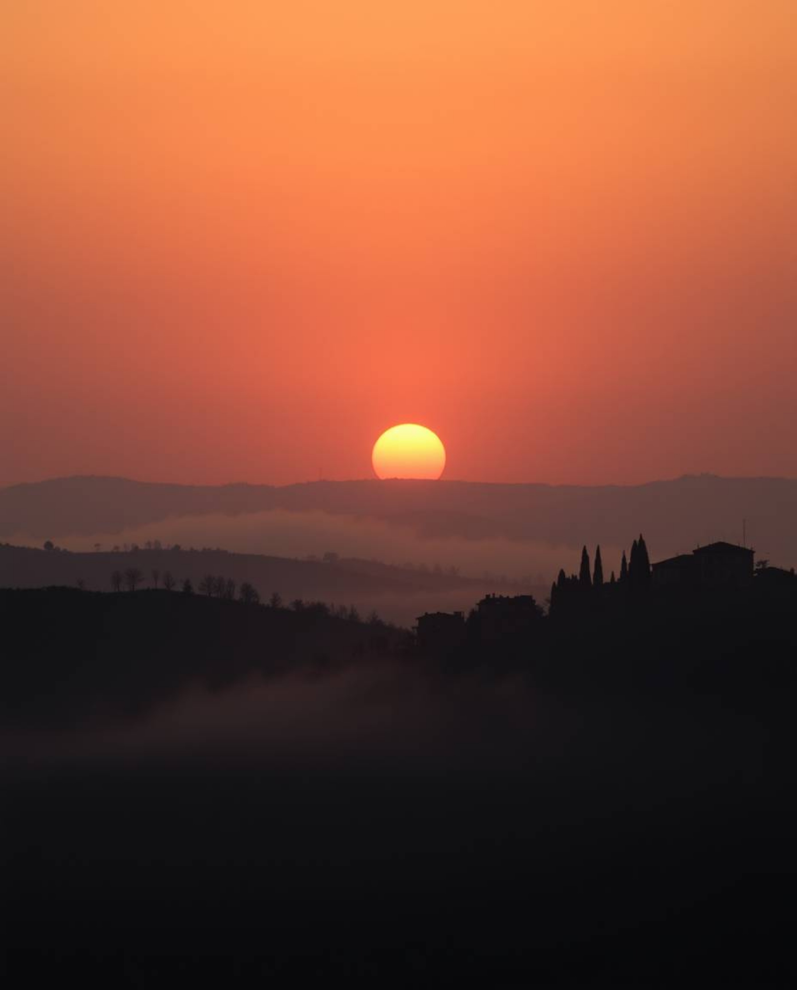 A moody style photograph of a sunset over misty Tuscan hills. Warm golden hour light, low contrast, soft light, just after su