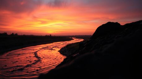 Experience the breathtaking beauty of a winding river illuminated by a dramatic orange-pink sunset. This extreme macro close-