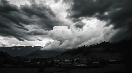 A timeless, elegant black and white photograph depicts a cozy village nestled in a valley, dramatically contrasted against a 