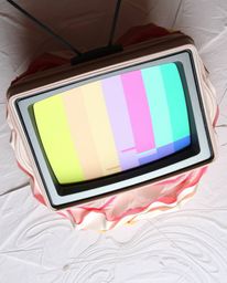 An overhead bird's eye view presents a layered papier-mâché creation, featuring a retro-style TV screen displaying glitch sta