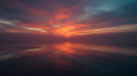 A captivating image showcasing a smooth gradient transition of a dramatic, cinematic sunset reflected in a calm pond.  The fi