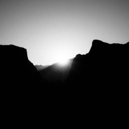 A captivating black and white photograph showcasing a silhouetted mountain valley at sunset.  The strong backlighting creates