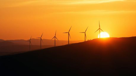 A breathtaking cinematic image captures a vibrant sunset casting a warm golden glow behind a row of wind turbines perched ato