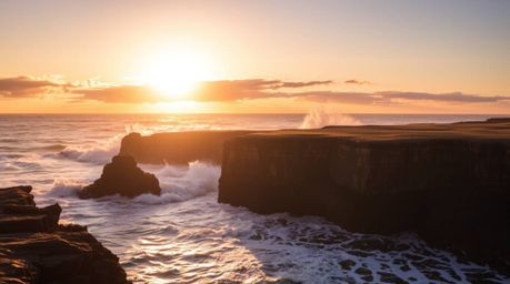 Witness the raw power and beauty of nature as waves crash against rugged cliffs beneath a blazing sunset sky. This scene is c