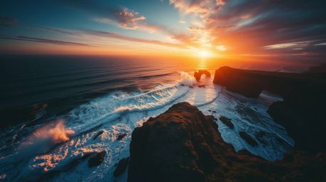 A stunning overhead shot captures the dramatic power of waves crashing against cliffs at sunset. High-contrast, low-key light