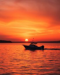 A boat drifts serenely on a lake at sunset, completely bathed in the warm hues of red, orange, and yellow. This peaceful imag
