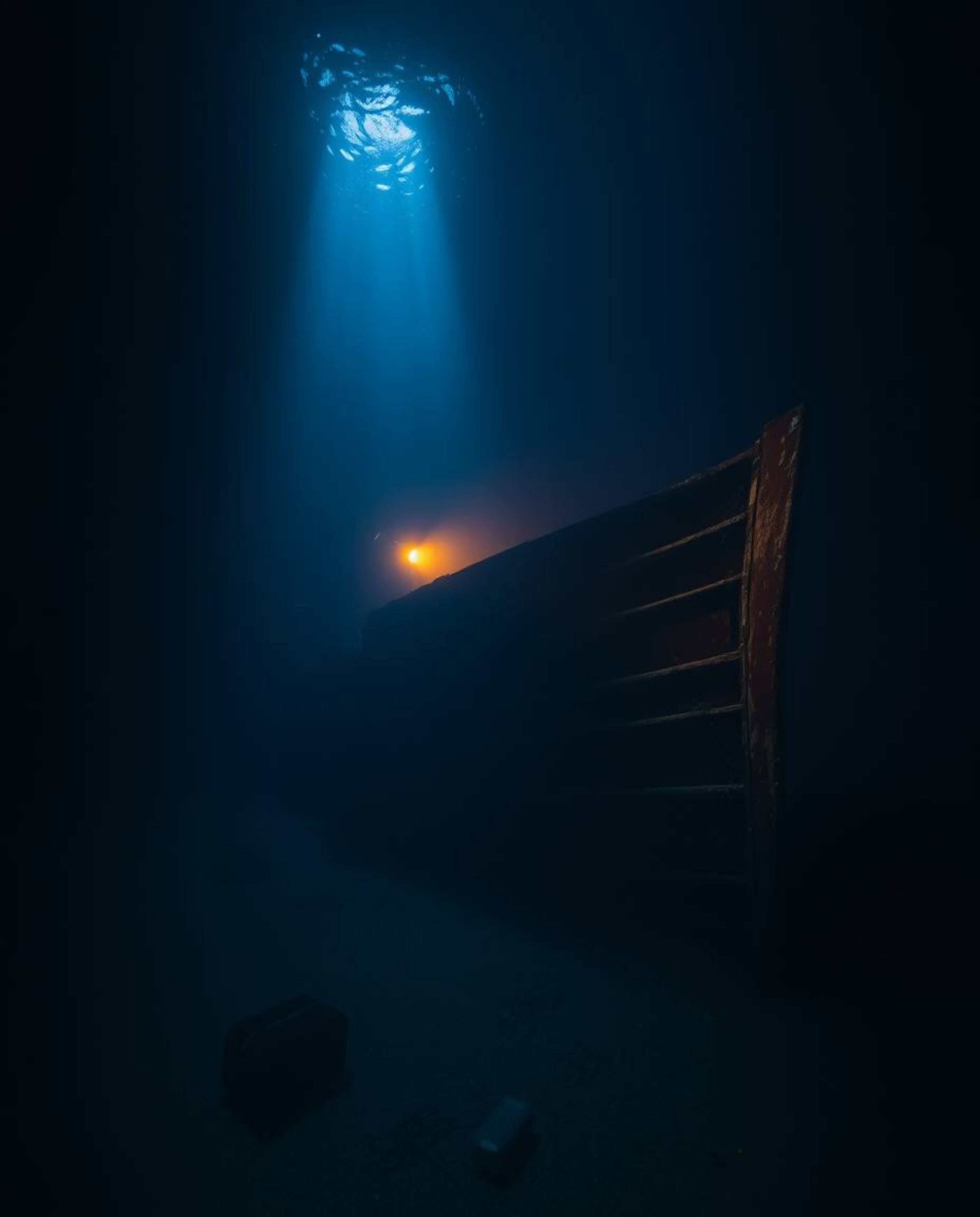 Discover breathtaking fine art photography of a shipwreck illuminated deep underwater.  The image features warm, soft light, 