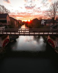 A photograph taken from an overhead bird's-eye view showcases a warm-toned old wooden bridge crossing a river during a vibran
