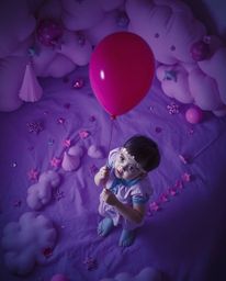 A captivating overhead shot depicts a child holding a balloon in a dreamlike scene.  The image is infused with deep ultraviol