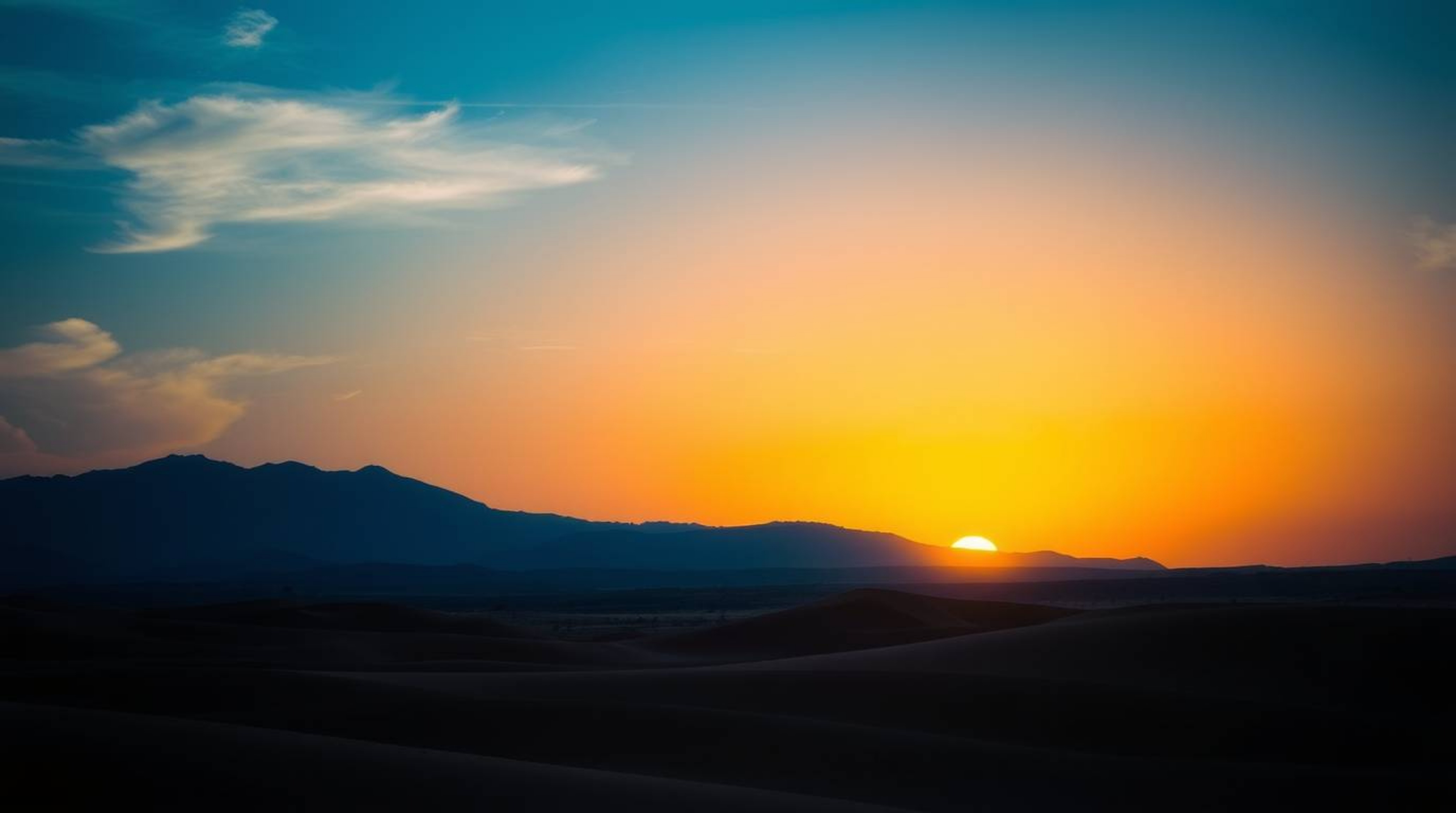 A captivating high-contrast photograph showcases a dramatic sunset over golden desert dunes.  Cool colors of blues, greens, a