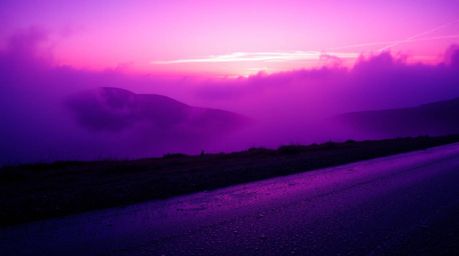 Experience the captivating beauty of deep ultraviolet hues and fog-covered hills bathed in the golden light of a setting sun.