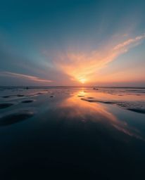 A cinematic photograph captures a sunset sky mirrored in the tidal pools on a beach, taken from a dramatic low-angle perspect