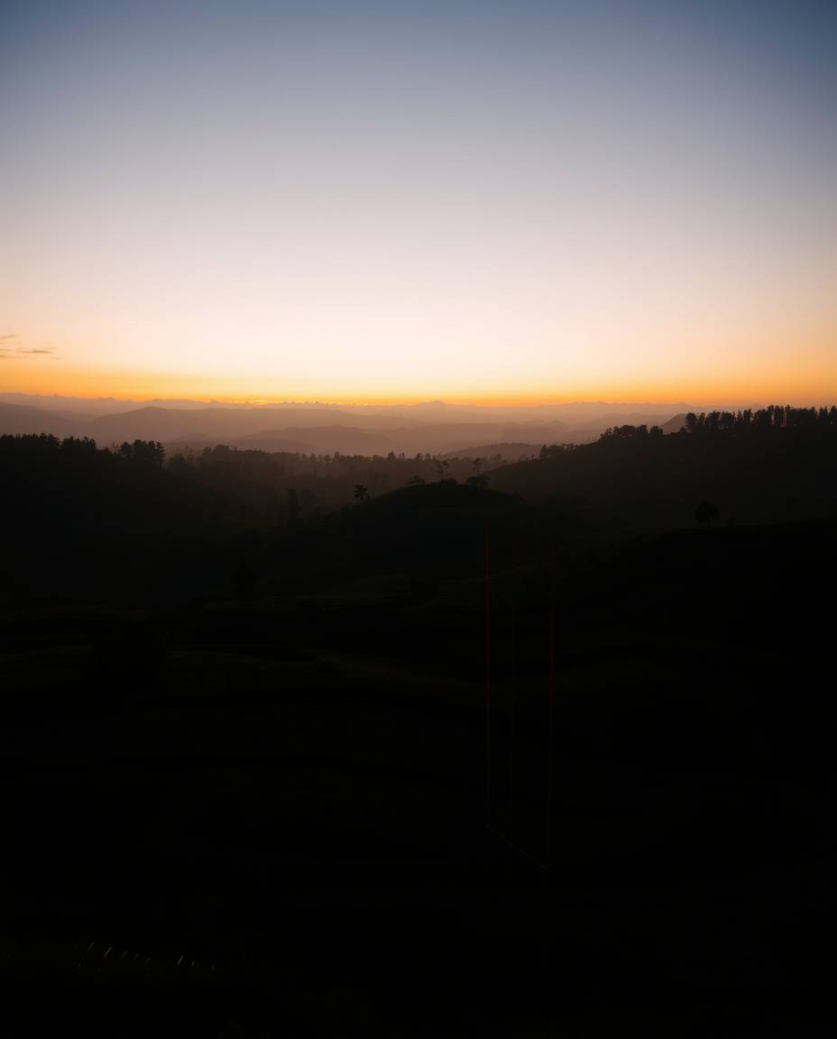 A long exposure photograph from a high-angle perspective captures silhouetted tea plantations at sunset. The use of backlight