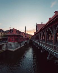 An architectural color photograph captures an old wooden bridge over a river at sunset, taken with a wide-angle lens. The com