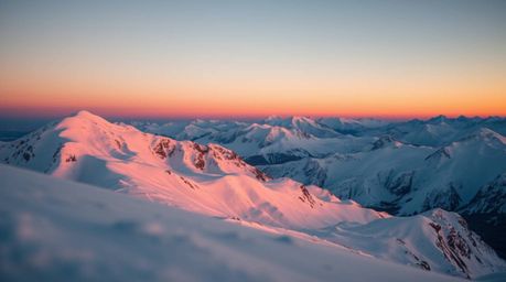 Experience the breathtaking beauty of snow-covered mountains bathed in the soft, warm glow of a pastel sunset. This close-up 