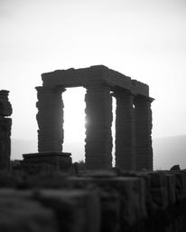 A classic black and white photograph captures a soft, cinematic image of ancient stone ruins at sunset. The use of soft focus