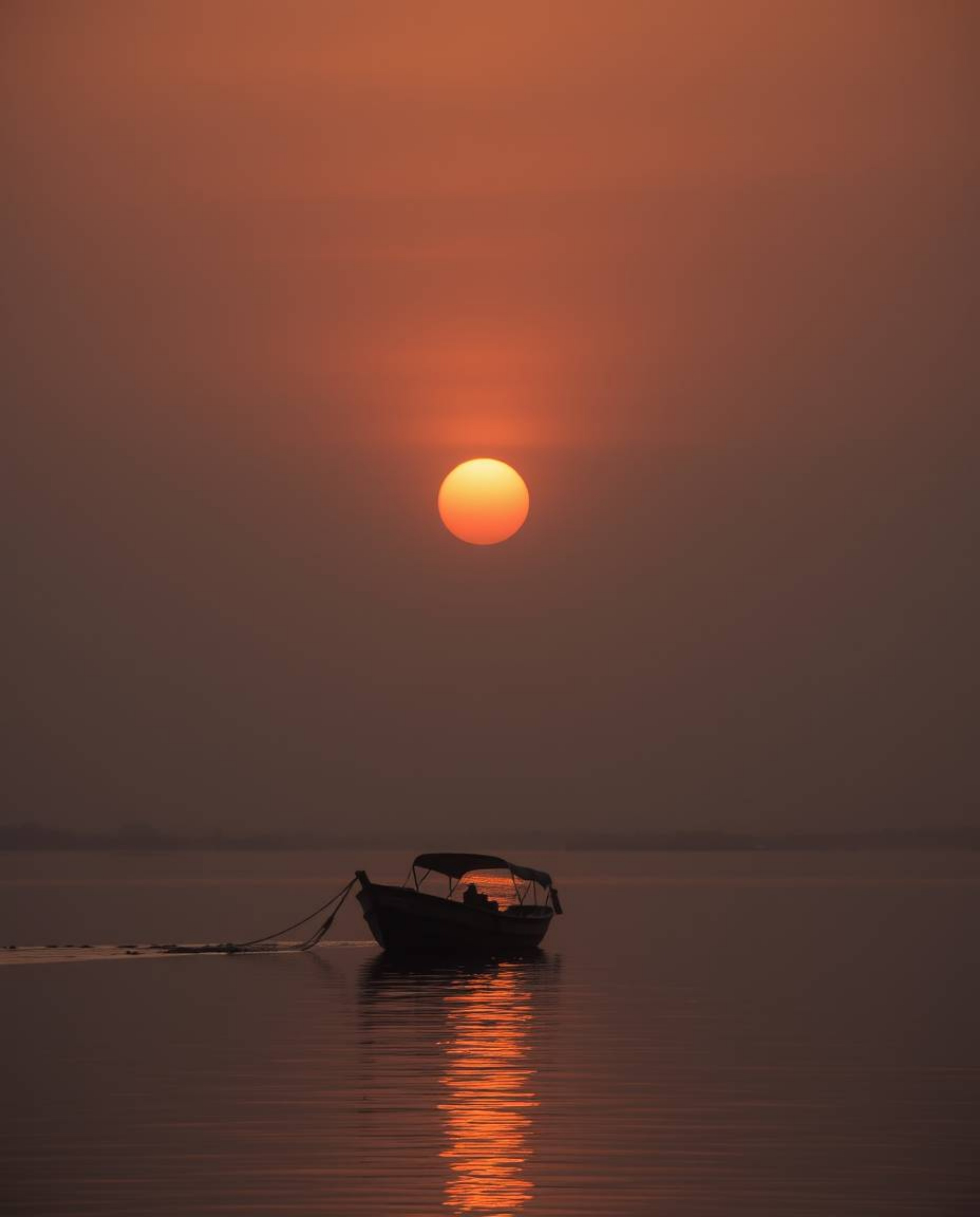 A moody golden hour image depicting a boat drifting on a lake at sunset. The soft light with low contrast evokes a serene and