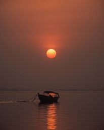 A moody golden hour image depicting a boat drifting on a lake at sunset. The soft light with low contrast evokes a serene and