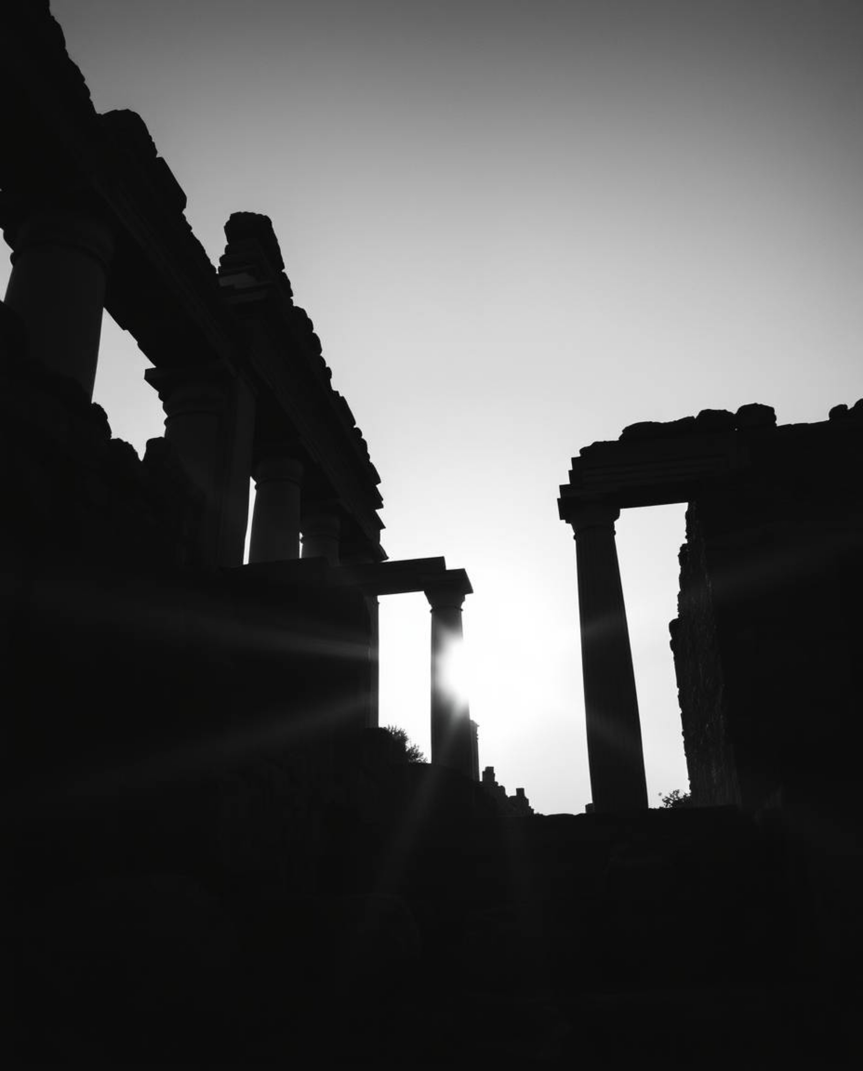 A classic black and white low-angle shot dramatically depicts ancient stone ruins at sunset. This perspective, looking upward