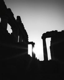 A classic black and white low-angle shot dramatically depicts ancient stone ruins at sunset. This perspective, looking upward