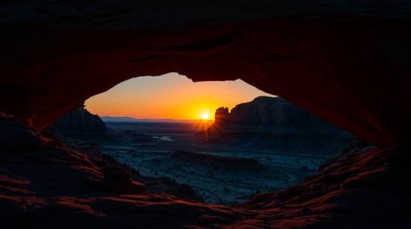 A luxurious and vibrant photograph capturing a desert sunset as viewed through a natural rock arch. The image features rich, 