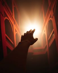 A captivating architectural color photograph captures a hand reaching towards a soft, hazy light emerging from darkness. The 