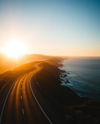 This is a dramatic, cinematic-style photograph of a winding coastal highway at sunset. The image is characterized by its use 