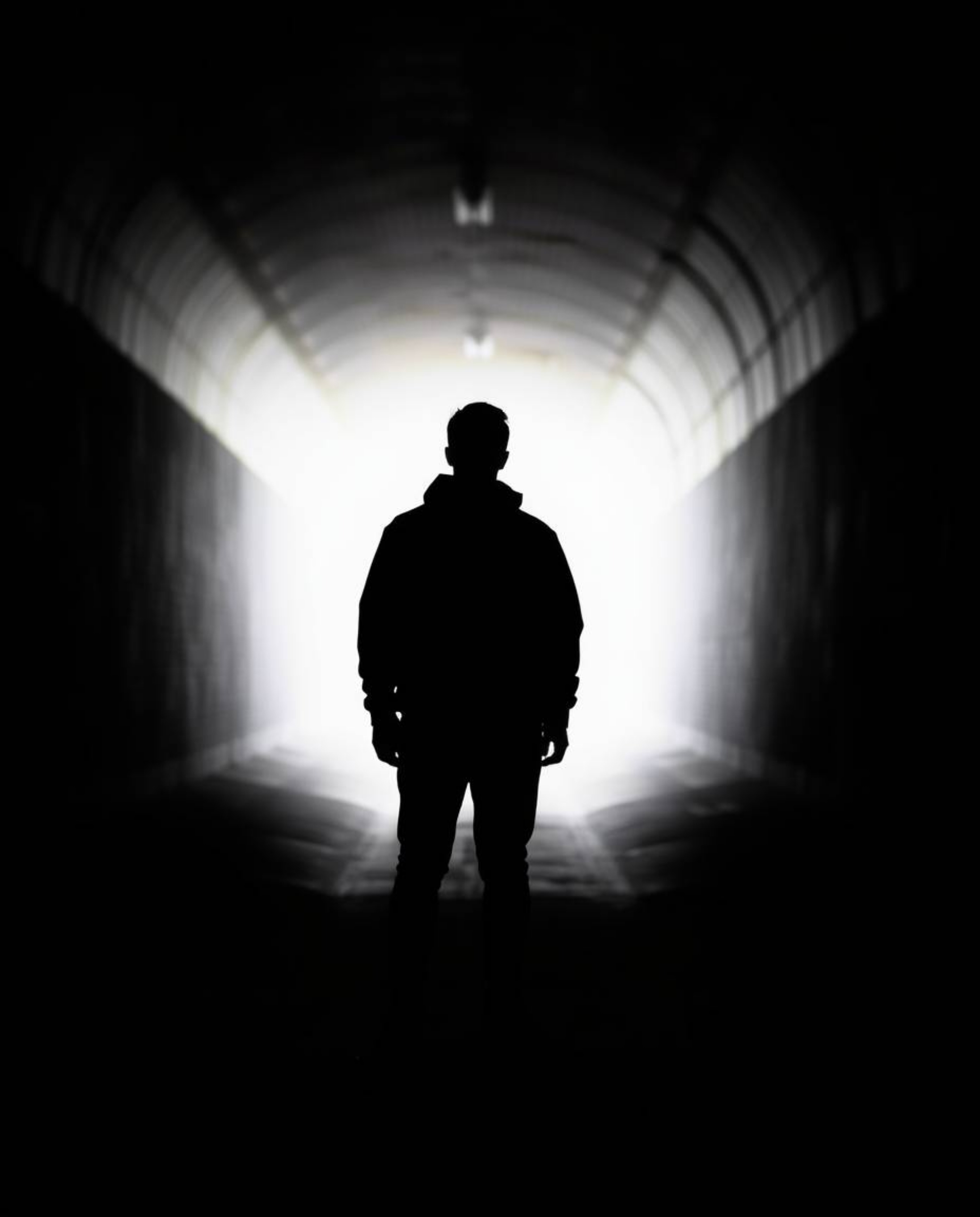 A striking silhouette photograph captures a person standing at the tunnel's edge, bathed in backlighting. The strong light so