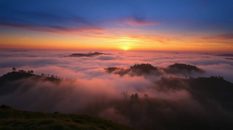 A stunning high-resolution stock photo depicting fog-covered hills at sunset. The image features dramatic lighting, high cont