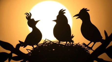 A delightful scene depicting silhouetted, layered papier-mâché cartoon birds diligently building a nest against a backlightin