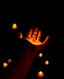 A compelling image featuring a hand reaching towards light emanating from the darkness, illuminated by warm candlelight. The 