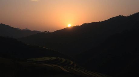 This image captures a striking sunset over rice terraces nestled in the mountains, utilizing contrasting chiaroscuro lighting